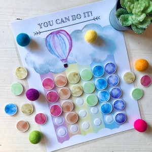 Op de afbeelding: Een kleurrijk regenboog-thema activiteitenbord met de tekst "YOU CAN DO IT!" en een illustratie van een luchtballon. Het bord heeft een verscheidenheid aan kleurrijke cirkels met verschillende patronen en texturen.