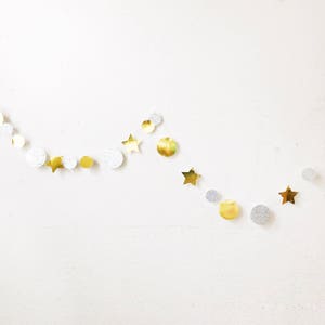 May include: A decorative garland featuring a repeating pattern of gold metallic stars, silver glitter circles, and smooth gold circles strung together on a thin white cord, creating a festive arrangement of alternating shapes and textures.