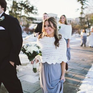 May include: A wedding party walks down a snow-covered path. The bride and bridesmaids wear gray dresses and white crocheted shawls. The groomsmen wear black tuxedos and carry bouquets of white flowers.