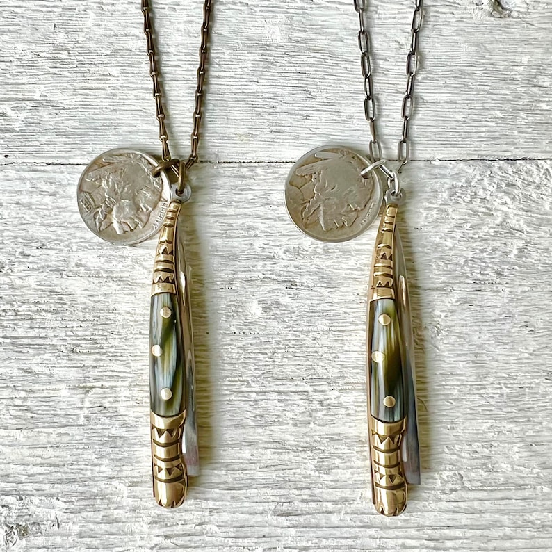 May include: Two necklaces with silver coins and gold-toned pocket knives. The pocket knives have a green and white patterned handle with gold accents.