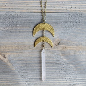 May include: A gold necklace with two hammered crescent moon pendants and a clear quartz crystal pendant.