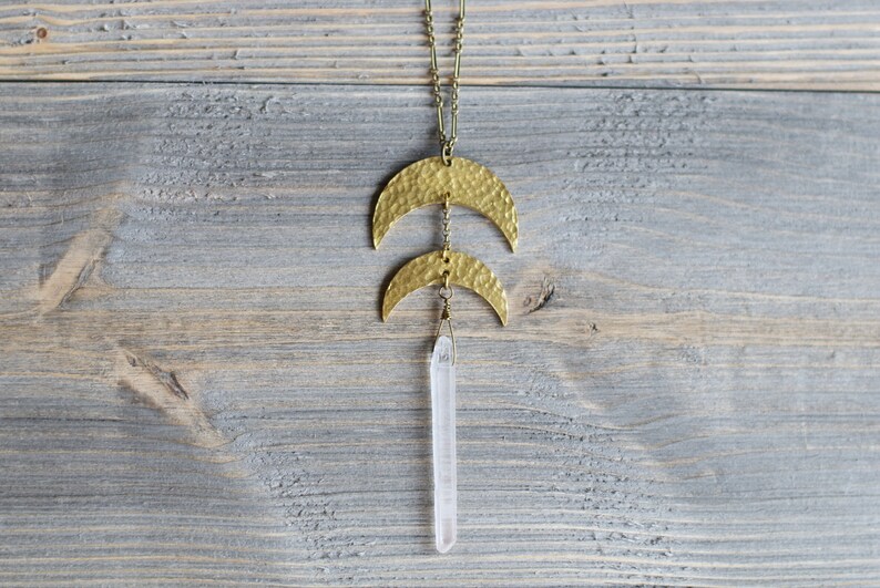 May include: A gold necklace with two hammered crescent moon pendants and a clear quartz crystal pendant.