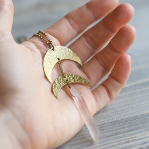 May include: A gold necklace with two hammered crescent moon pendants and a clear quartz crystal pendant.