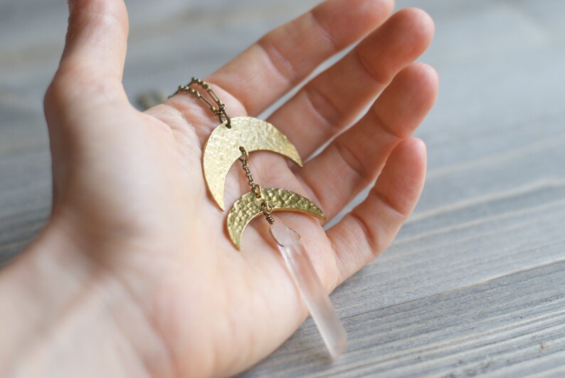 May include: A gold necklace with two hammered crescent moon pendants and a clear quartz crystal pendant.
