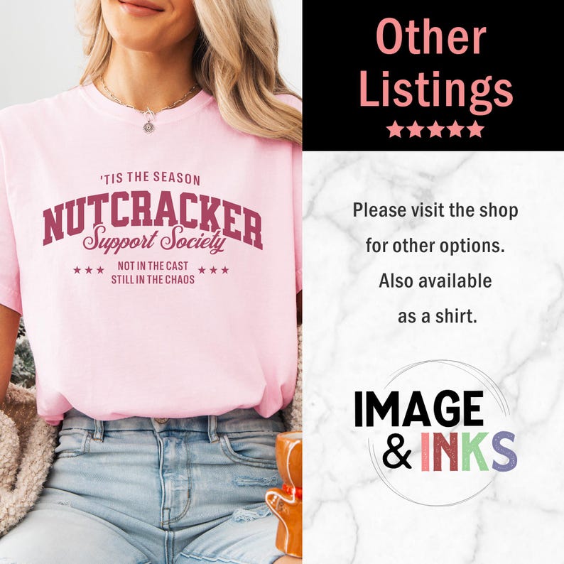 May include: A light pink short-sleeved t-shirt featuring the maroon text 'TIS THE SEASON NUTCRACKER Support Society NOT IN THE CAST STILL IN THE CHAOS with star accents. The shirt is paired with blue denim jeans and a silver chain necklace.