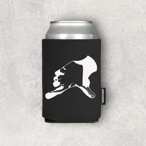May include: Black neoprene can cooler with a white silhouette of a hand making a gesture. The cooler has the text "KOZIE" printed on the side.