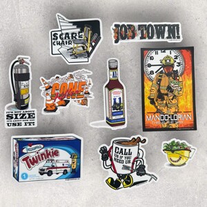 May include: A collection of stickers with various designs. Includes a fire extinguisher, a bottle of sauce, a box of Twinkies, and a sticker that says "MANDO-LORIAN THIS IS THE WAY". Other stickers feature text like "JOB TOWN!" and "CALL US IF YOU NEED US."
