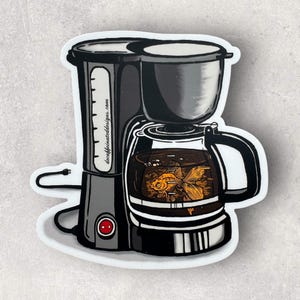 May include: A sticker featuring a black and gray coffee maker with a glass carafe. Inside the carafe is a goldfish swimming in dark liquid. The sticker has a white border and the text "decaffeinateddesigns.com".