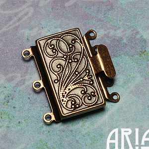 May include: A bronze-colored metal jewelry clasp with a decorative floral design. The clasp has four loops for attaching jewelry chains or cords.