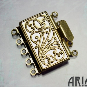 May include: Gold-tone metal jewelry clasp with a decorative floral design and five loops for attaching chains or cords.