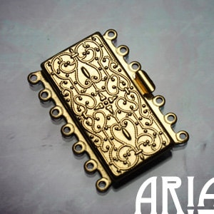 May include: Gold-toned metal clasp with an ornate design and multiple loops for attaching jewelry.