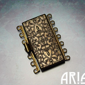 May include: Gold-toned metal clasp with a decorative filigree design and multiple loops for attaching jewelry chains or cords.