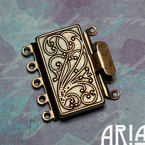 May include: A gold-toned metal jewelry clasp with a decorative floral design. The clasp has five loops for attaching jewelry chains or cords.