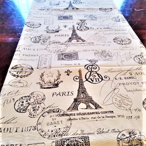 May include: A beige table runner with a repeating pattern of black and white stamps featuring the Eiffel Tower, Parisian text, and other vintage designs.