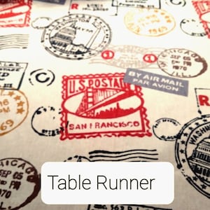May include: A white table runner with a vintage postage stamp design. The stamps feature images of the Golden Gate Bridge, the Capitol Building, and other iconic landmarks. The text "Table Runner" is printed on the runner.