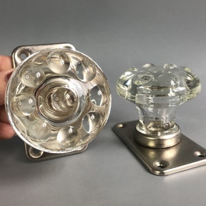 May include: Two clear glass door knobs with a textured surface. The knobs are attached to silver metal plates.