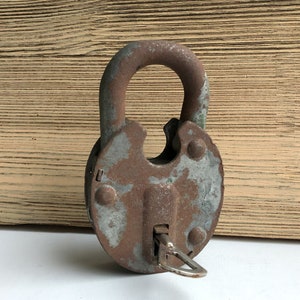 May include: A rusty metal padlock with a keyhole and a silver key. The padlock has a worn, aged appearance.
