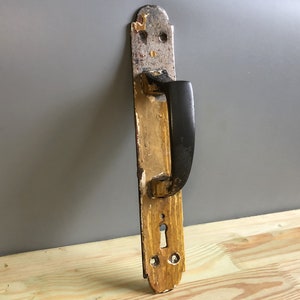 以下が含まれることがあります： 黒いハンドルと金色の金属プレートが付いたヴィンテージのドアハンドル。プレートには鍵穴と装飾的なディテールがあります。