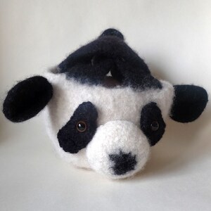 Peut inclure: Un panier en crochet en forme de panda blanc et noir avec des yeux noirs et un nez noir.