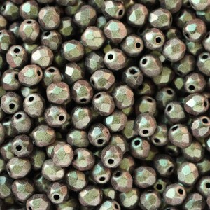 May include: Close-up of a collection of faceted beads. The beads are a muted, metallic grey-green colour with a textured, multi-faceted surface. Each bead has a hole for stringing, suitable for jewellery making or crafts.
