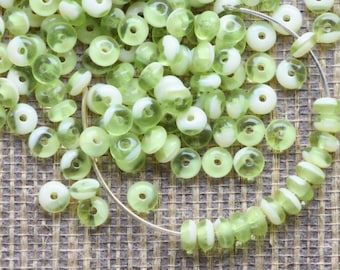 May include: A collection of light green and white glass beads with a hole in the center. Some beads are strung on a silver wire. The beads have a translucent quality, and the color is reminiscent of spring. The beads are small and round.