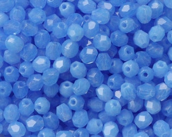 May include: A pile of faceted, light blue beads. Each bead has multiple flat surfaces that catch the light, creating a sparkling effect. The beads are small and uniform in size, suitable for jewelry making or crafts.