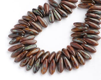 May include: Strands of brown, teardrop-shaped beads with iridescent green and blue accents. The beads are strung together, forming a curved shape, ideal for jewelry making. The beads have a glossy finish and are arranged against a white background.