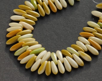 May include: Strand of teardrop-shaped beads in shades of ivory, green, yellow, and orange. The beads are strung together, creating a curved shape against a dark gray background. The beads are smooth and glossy.