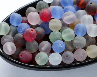 May include: A collection of frosted glass beads in various colors, including red, blue, green, and white, are displayed in a black dish. The beads are round and have a matte finish, suitable for jewelry making or craft projects.