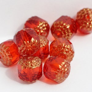May include: A selection of red glass beads with gold detailing. The beads have a faceted design and textured gold sections. These decorative beads are suitable for jewellery making and craft projects. Each bead is approximately 1 cm in diameter.