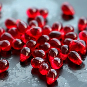Puede incluir: Primer plano de numerosos objetos brillantes, de color rojo intenso, en forma de lágrima, dispersos sobre una superficie oscura. Los objetos son translúcidos, reflejan la luz y crean reflejos. La imagen transmite una sensación de color y textura ricos.