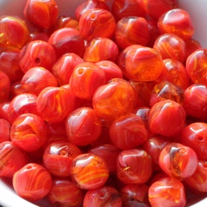 May include: A collection of vibrant, translucent orange beads with a marbled effect. The beads are cube-shaped with rounded edges and a hole for stringing. The beads are in a white bowl, ideal for jewellery making.