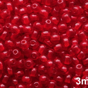 Peut inclure: Gros plan sur un tas de petites perles rouges translucides. Les perles sont cylindriques avec des bords arrondis et un trou au centre. Le texte "3mm" est visible, indiquant la taille des perles, soit environ 0,3 cm.