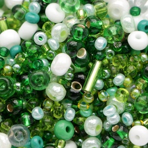 May include: A collection of assorted beads in shades of green, white, and teal. The beads vary in size and shape, including round, tube, and irregular forms. Some beads are transparent, while others are opaque, creating a mix of textures and colors.