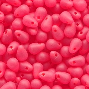 May include: A close-up of many pink, teardrop-shaped beads. Each bead has a small hole at the top. The beads are scattered across the frame and are a solid, matte pink colour.