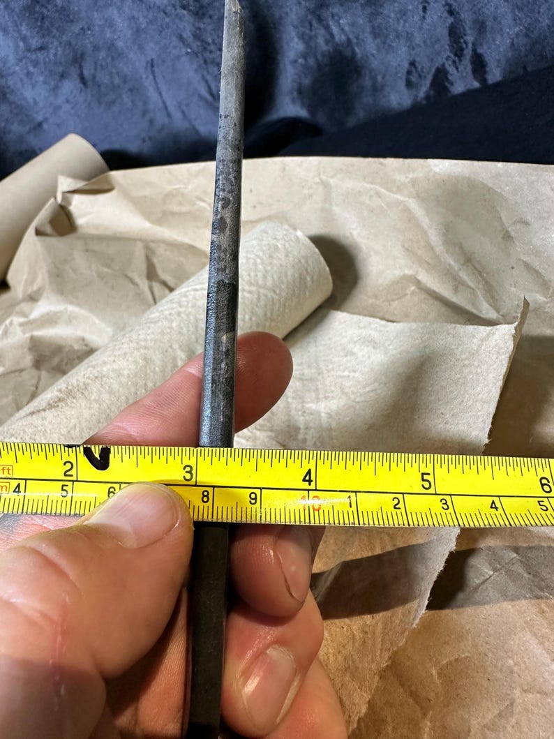 Puede incluir: Una herramienta de metal, de aproximadamente 7,6 cm de largo, se sostiene junto a una cinta m&eacute;trica amarilla. La herramienta tiene un aspecto oscuro y desgastado. La cinta m&eacute;trica muestra medidas en pulgadas.