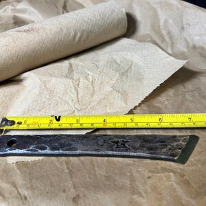 Puede incluir: Una hoja de metal forjada a mano con una cinta m&eacute;trica amarilla y un rollo de toallas de papel marr&oacute;n. La hoja mide aproximadamente 15 cm de largo. La cinta m&eacute;trica muestra pulgadas y fracciones de pulgada.