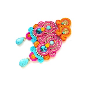 May include: A pair of colorful earrings with turquoise stones and a pink, orange, and blue design. The earrings are made with a technique called kumihimo, which involves braiding threads together to create intricate patterns.