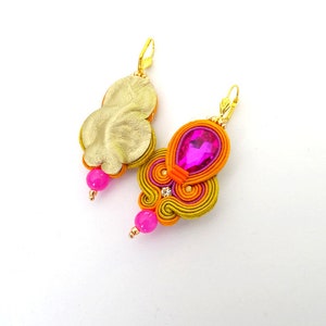 May include: A pair of earrings with a gold-colored metal base and a pink and orange fabric design. The earrings feature a pink crystal and a pink bead.