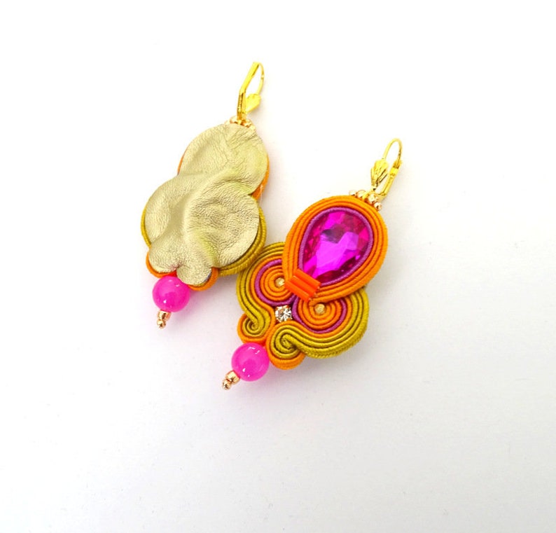 May include: A pair of earrings with a gold-colored metal base and a pink and orange fabric design. The earrings feature a pink crystal and a pink bead.