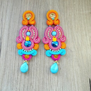 May include: A pair of long, colorful earrings with a pink, orange, and blue design. The earrings feature a turquoise stone at the bottom and a variety of smaller beads and rhinestones.