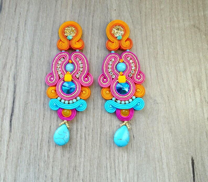May include: A pair of long, colorful earrings with a pink, orange, and blue design. The earrings feature a turquoise stone at the bottom and a variety of smaller beads and rhinestones.