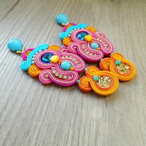 May include: A pair of colorful earrings with a pink, orange, and blue design. The earrings are made with a variety of beads and rhinestones.