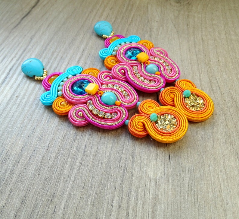 May include: A pair of colorful earrings with a pink, orange, and blue design. The earrings are made with a variety of beads and rhinestones.