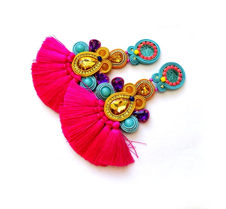 Pode incluir: Um par de brincos coloridos com borlas rosa, contas turquesa e amarelas e detalhes dourados.