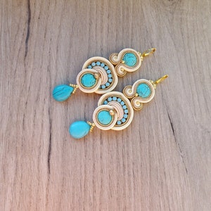 May include: A pair of dangle earrings with turquoise and white beads. The earrings are made of gold wire and have a delicate, intricate design.