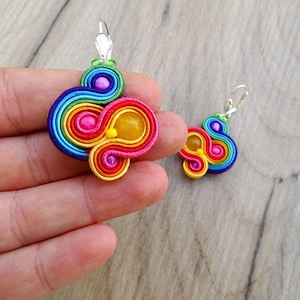 May include: Rainbow coloured earrings with a yellow, pink and purple bead accent. The earrings are made of a coiled rope-like material.