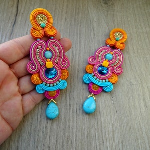 May include: A pair of long, colorful earrings with turquoise stones. The earrings are made of pink, orange, and blue thread and feature a variety of beads and rhinestones.