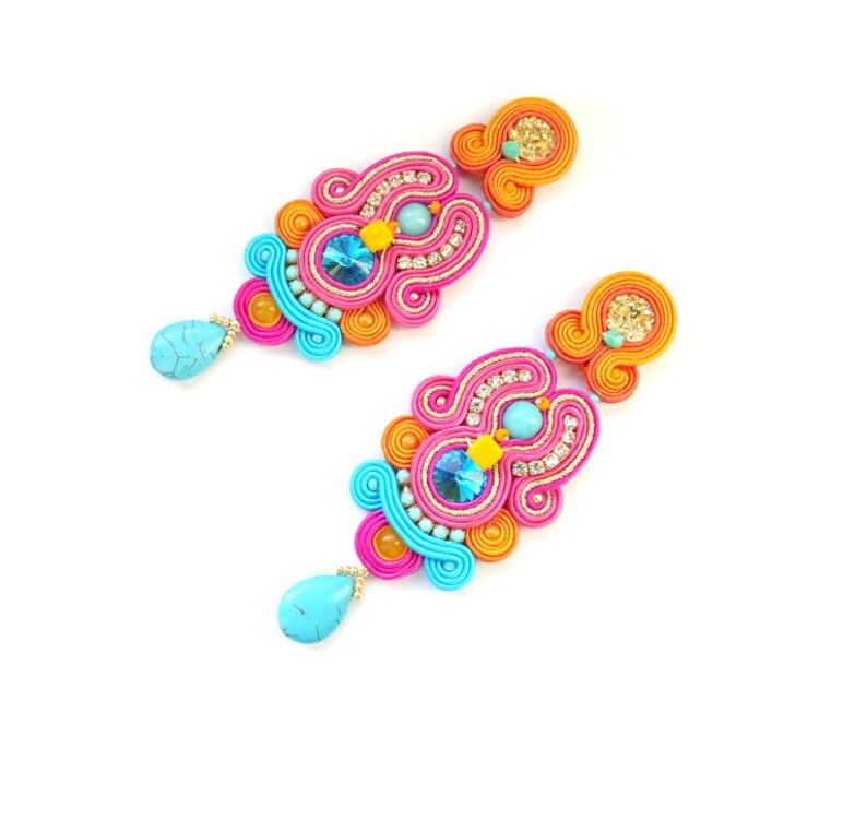 May include: A pair of colorful earrings with turquoise, pink, orange, and gold accents. The earrings are made of intricate woven threads and feature sparkling rhinestones.