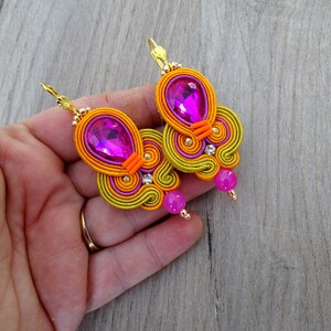 May include: A pair of earrings with a pink and orange swirl design. The earrings feature a large pink crystal and a smaller pink bead.